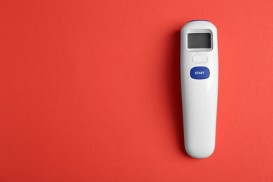 Photo of Modern non-contact infrared thermometer on red background, top view. Space for text