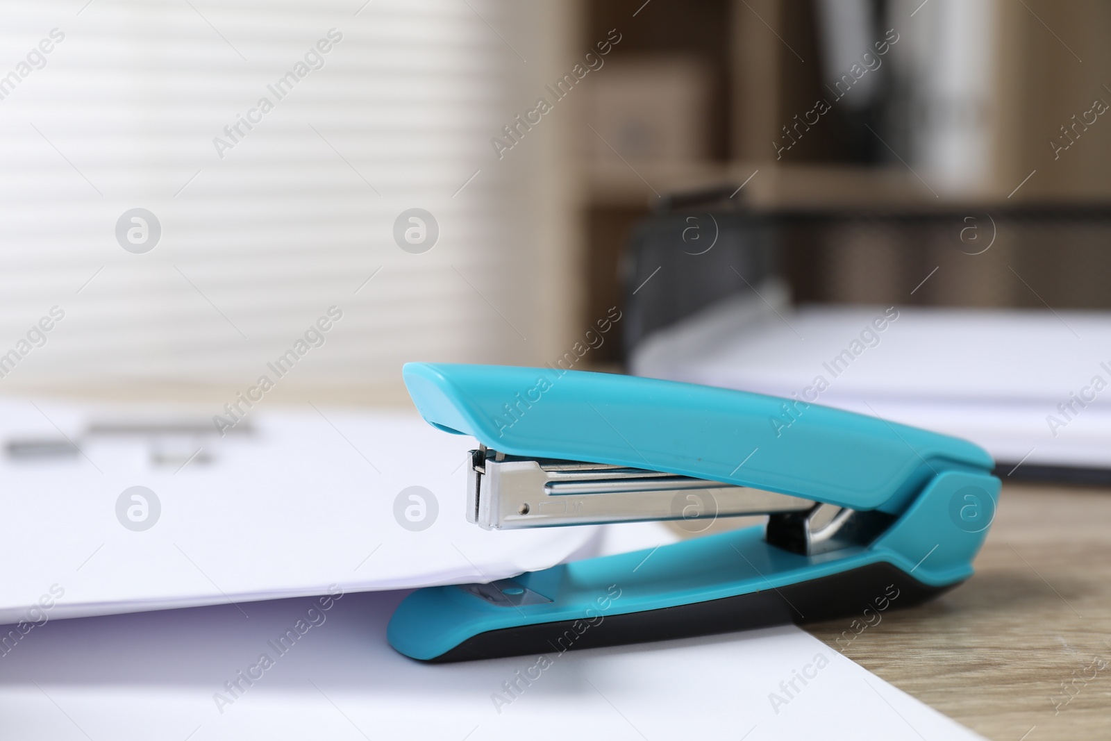 Photo of Stapler with papers on table indoors, closeup