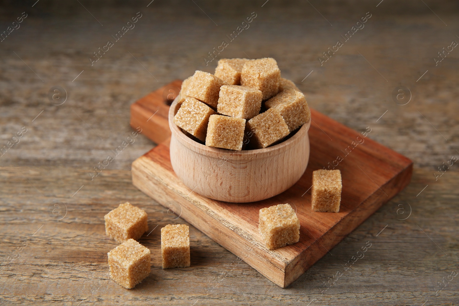 Photo of Brown sugar cubes in bowl on wooden table, closeup