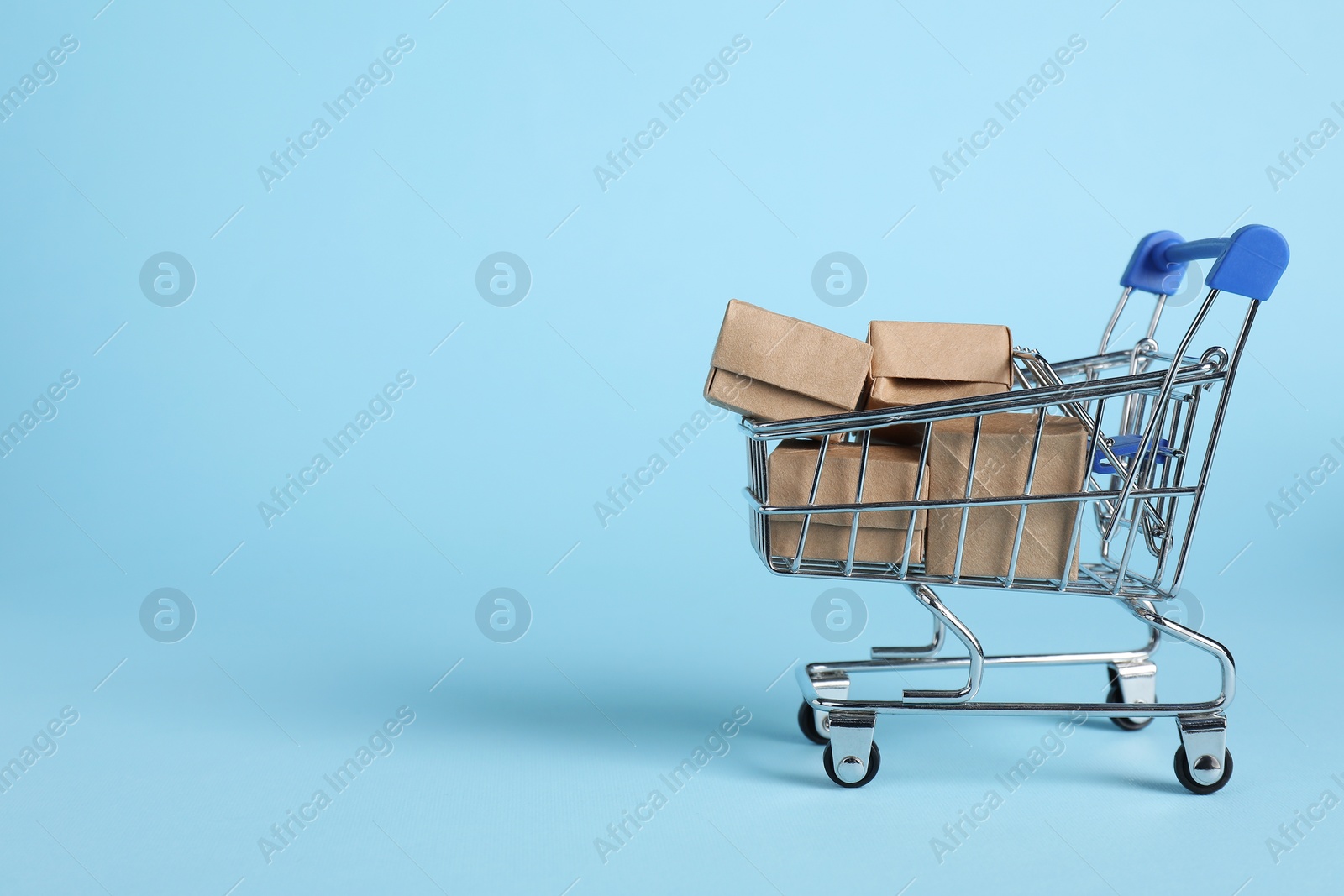 Photo of Small metal shopping cart with cardboard boxes on light blue background, space for text