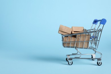 Photo of Small metal shopping cart with cardboard boxes on light blue background, space for text
