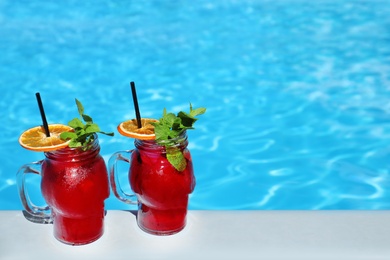 Mason jars with refreshing cocktail near swimming pool on sunny day. Space for text