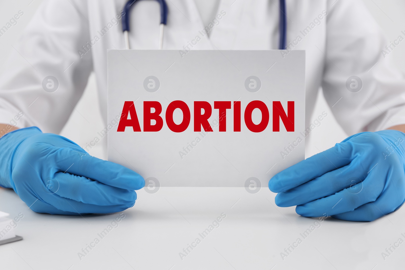 Image of Doctor holding paper card with word Abortion at white table, closeup