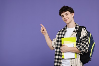 Portrait of student with backpack and notebooks pointing on purple background. Space for text