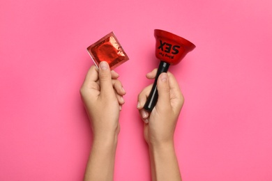 Woman with sex bell and condom on pink background, top view