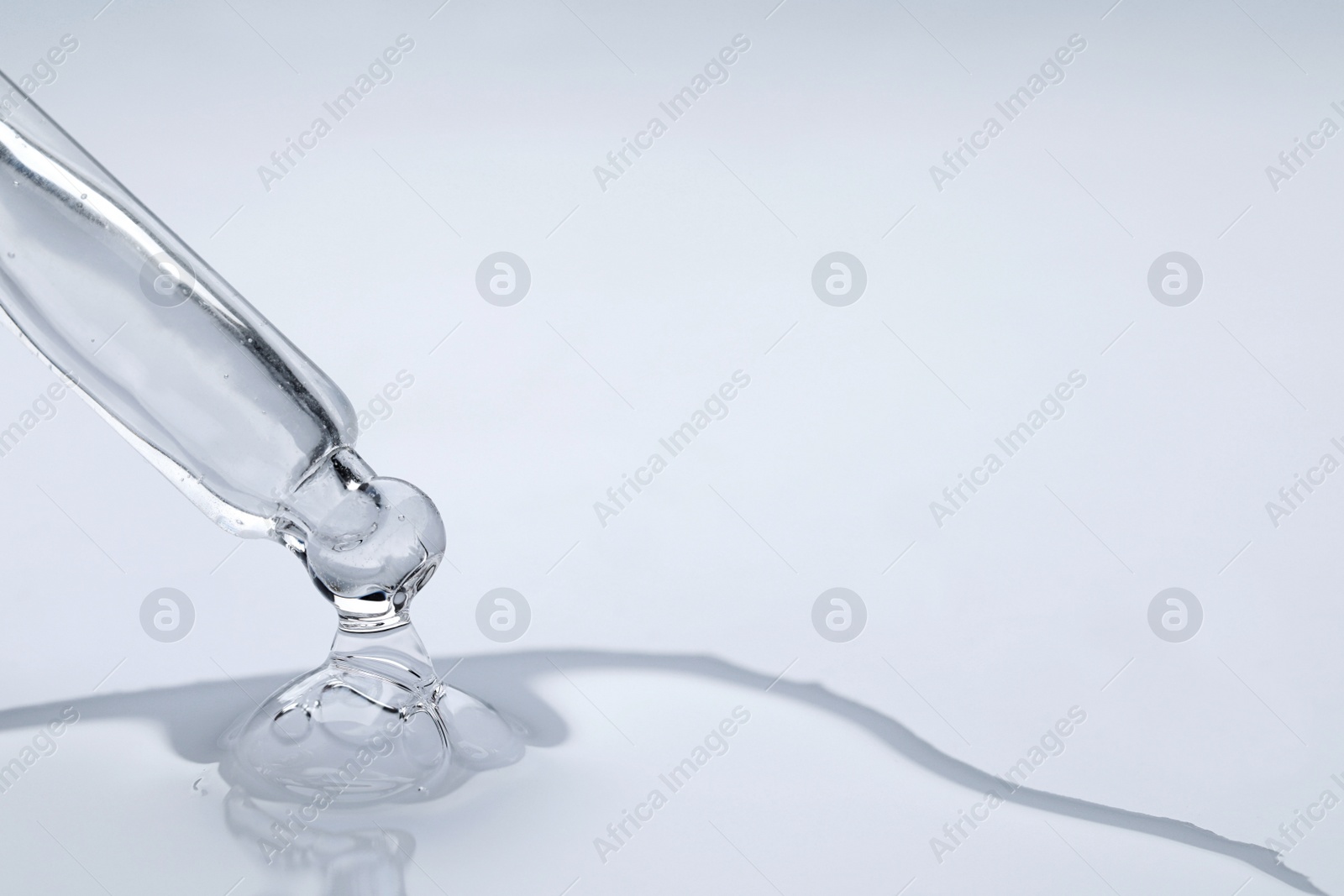 Photo of Dripping face serum from pipette on white background, closeup. Space for text