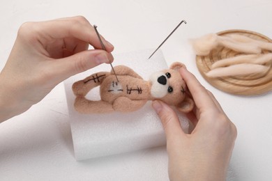 Photo of Woman felting toy bear from wool at white table, closeup