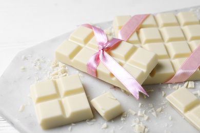 Photo of Tasty white chocolate with ribbons on marble board, closeup