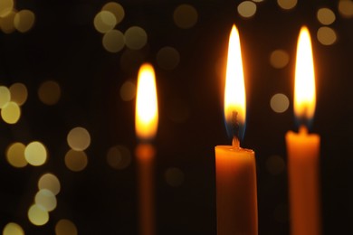 Burning candles on dark background with blurred lights, closeup. Bokeh effect