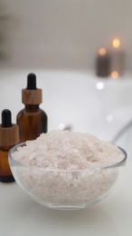 Photo of Glass bowl with bath salt and cosmetic products on white countertop indoors