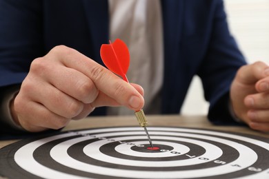 Business targeting concept. Man with dart aiming at dartboard at table, closeup