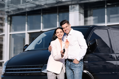 Happy couple with key near car on city street. Buying new auto