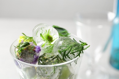 Glass of ice cubes with flowers on blurred background, closeup