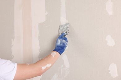 Photo of Man plastering wall with putty knife indoors, closeup. Home renovation