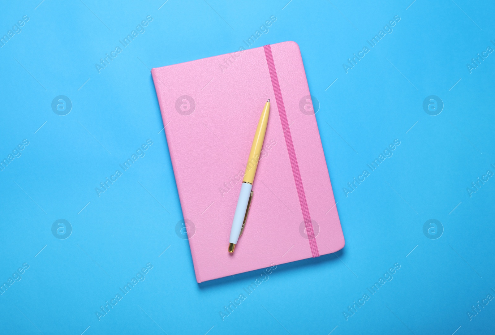 Photo of Closed pink notebook and pen on light blue background, top view