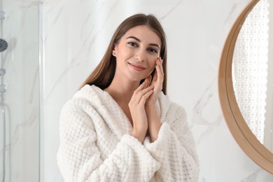 Photo of Young woman near mirror in bathroom. Skin care