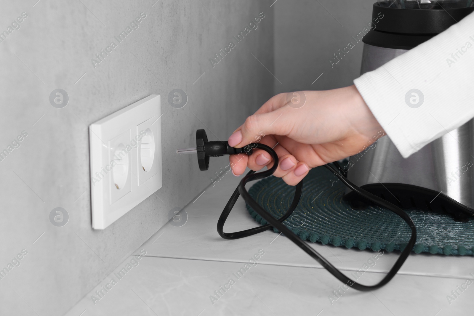 Photo of Woman plugging blender into socket at white table indoors, closeup