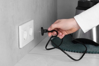 Woman plugging blender into socket at white table indoors, closeup