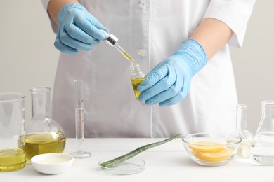 Scientist developing cosmetic oil at white table, closeup