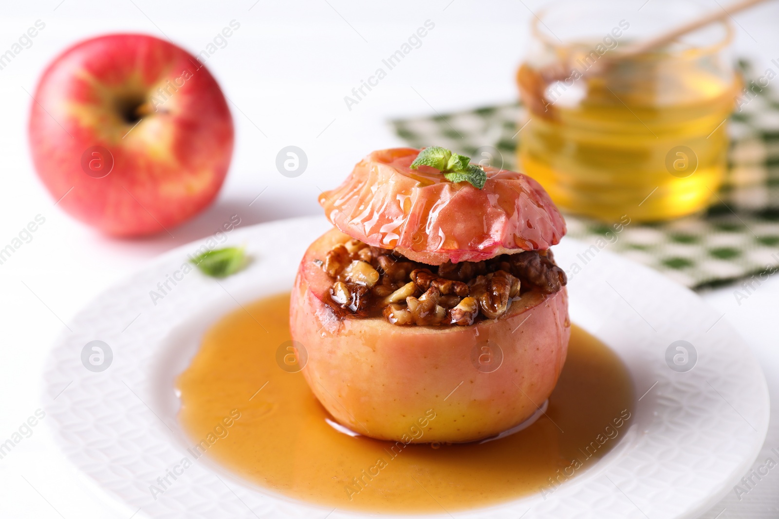 Photo of Tasty baked apple with nuts, honey and mint on white table, closeup