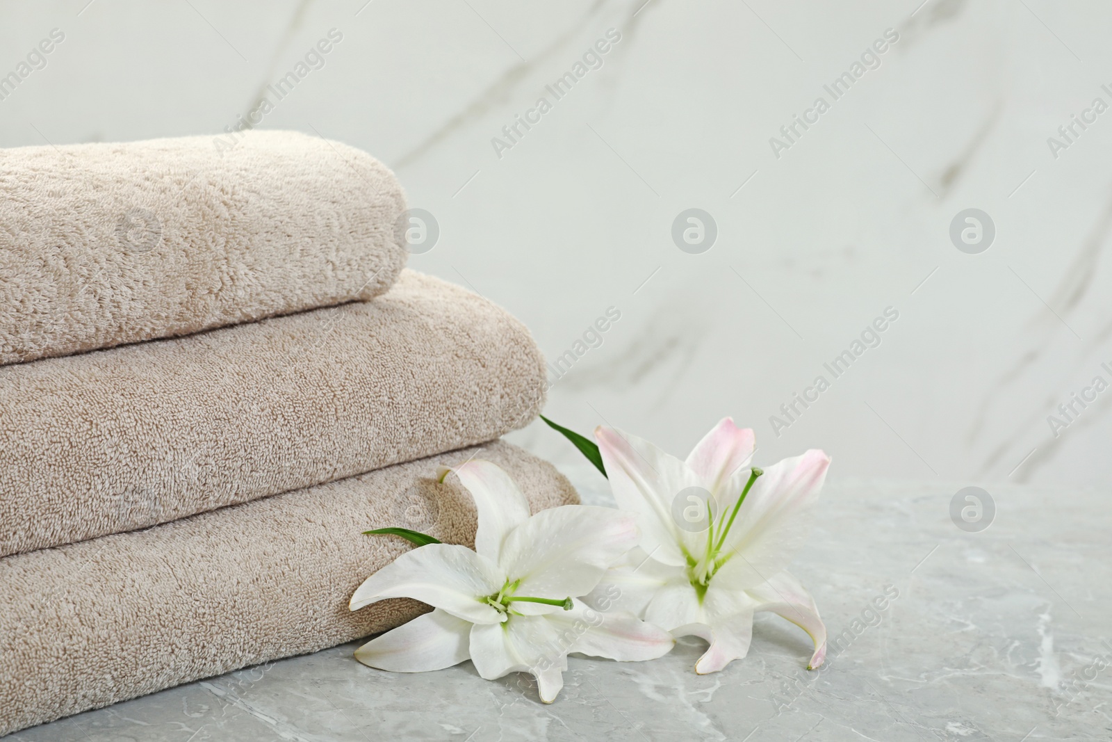 Photo of Stack of fresh towels with flowers on grey table against light background. Space for text