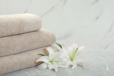 Photo of Stack of fresh towels with flowers on grey table against light background. Space for text