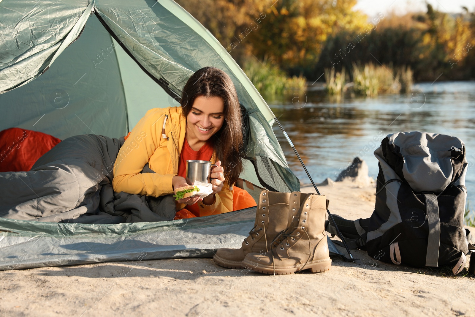 Photo of Young woman having breakfast in sleeping bag inside of camping tent