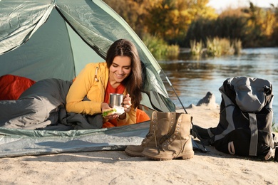 Young woman having breakfast in sleeping bag inside of camping tent