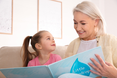 Mature woman with her little granddaughter reading book together at home
