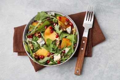 Tasty salad with persimmon, blue cheese, pomegranate and walnuts served on light grey table, top view