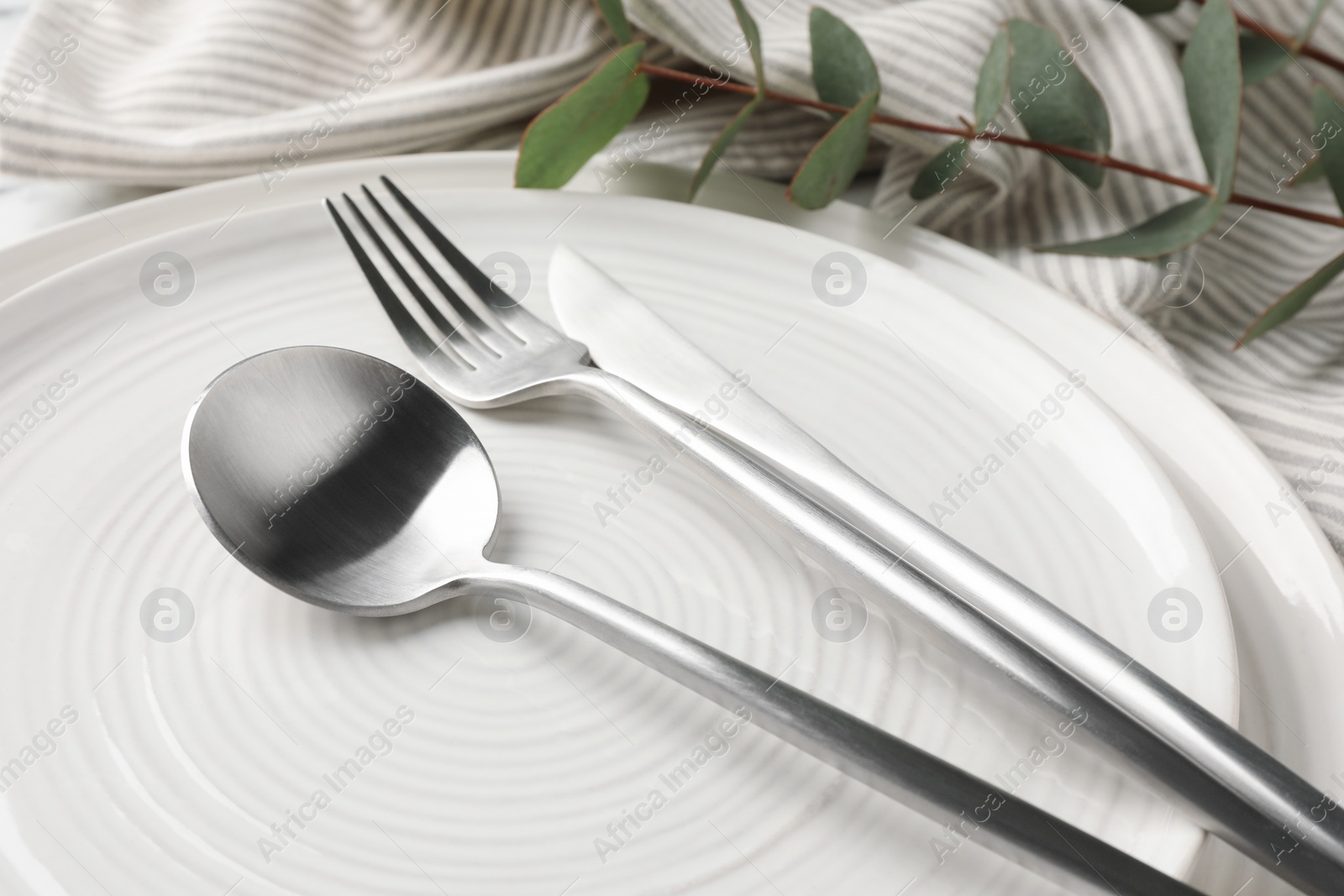 Photo of Stylish setting with cutlery, napkin, eucalyptus branch and plates on table, closeup