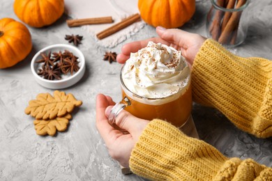 Photo of Woman holding cup of pumpkin spice latte with whipped cream at light grey table, closeup