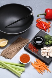 Photo of Wok, chopsticks and different products on grey table