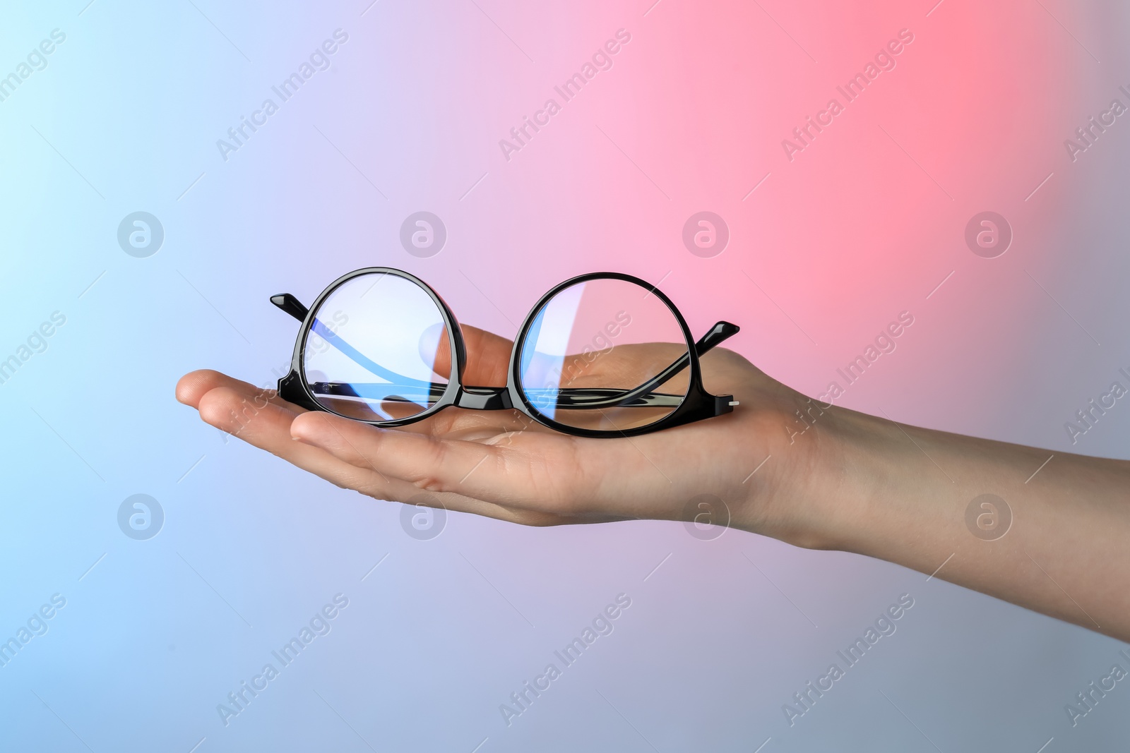 Photo of Woman holding glasses with black frame on color background, closeup