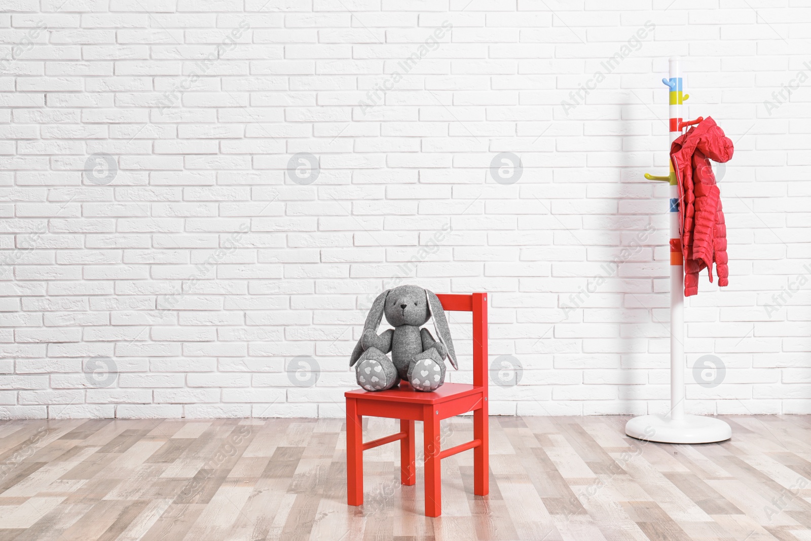 Photo of Stuffed toy rabbit on chair and clothes rack in child room. Space for text