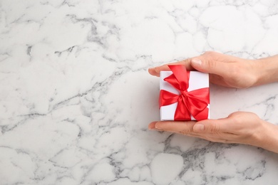Photo of Woman holding gift box at marble table, top view with space for text. Valentine's Day celebration