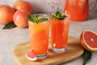 Photo of Tasty freshly made grapefruit juice, fruits and mint on light grey table