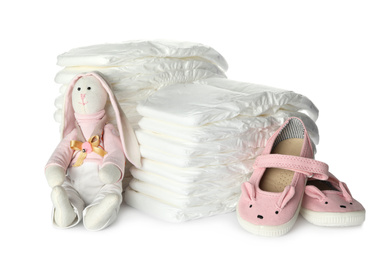Photo of Disposable diapers, toy bunny and child's shoes on white background