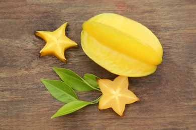 Cut and whole delicious ripe carambolas with leaves on wooden table, flat lay