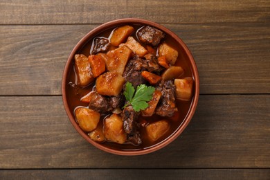 Photo of Delicious beef stew with carrots, parsley and potatoes on wooden table, top view