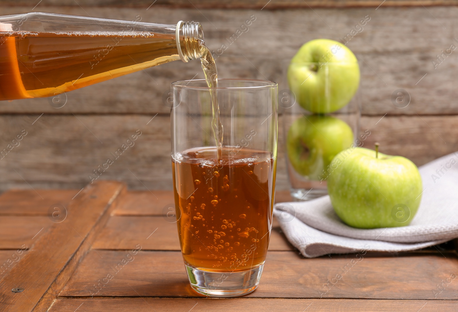 Photo of Pouring fresh apple juice from bottle into glass on wooden table