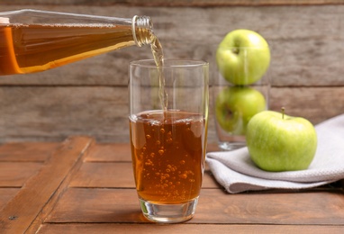 Pouring fresh apple juice from bottle into glass on wooden table