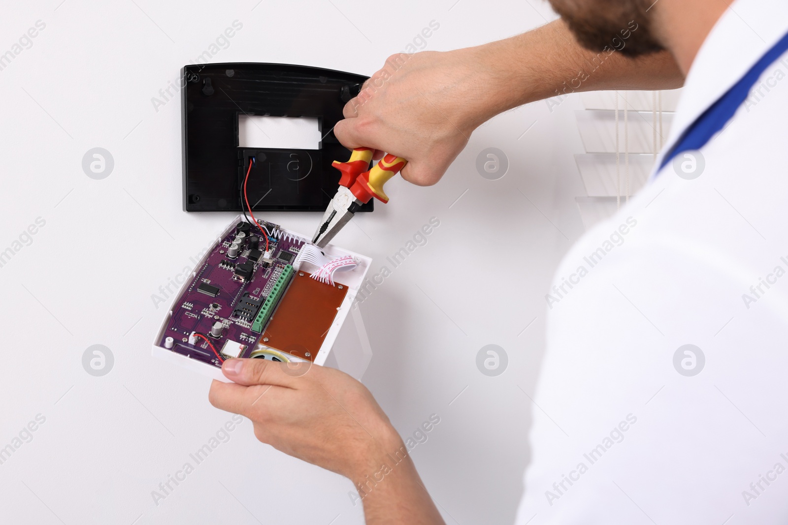 Photo of Man installing home security alarm system on white wall indoors, closeup