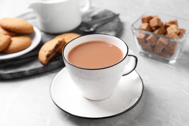 Delicious tea with milk in white cup near cookies on grey table