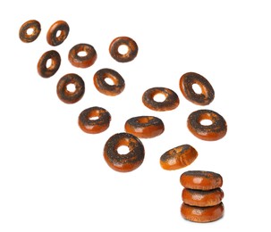 Many fresh bagels with poppy seeds falling onto stack on white background