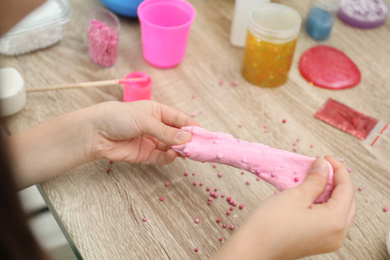 Photo of Little girl making homemade slime toy at table, closeup