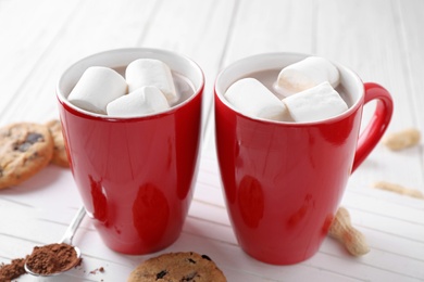 Cups of tasty cocoa with marshmallows and cookies on white wooden table