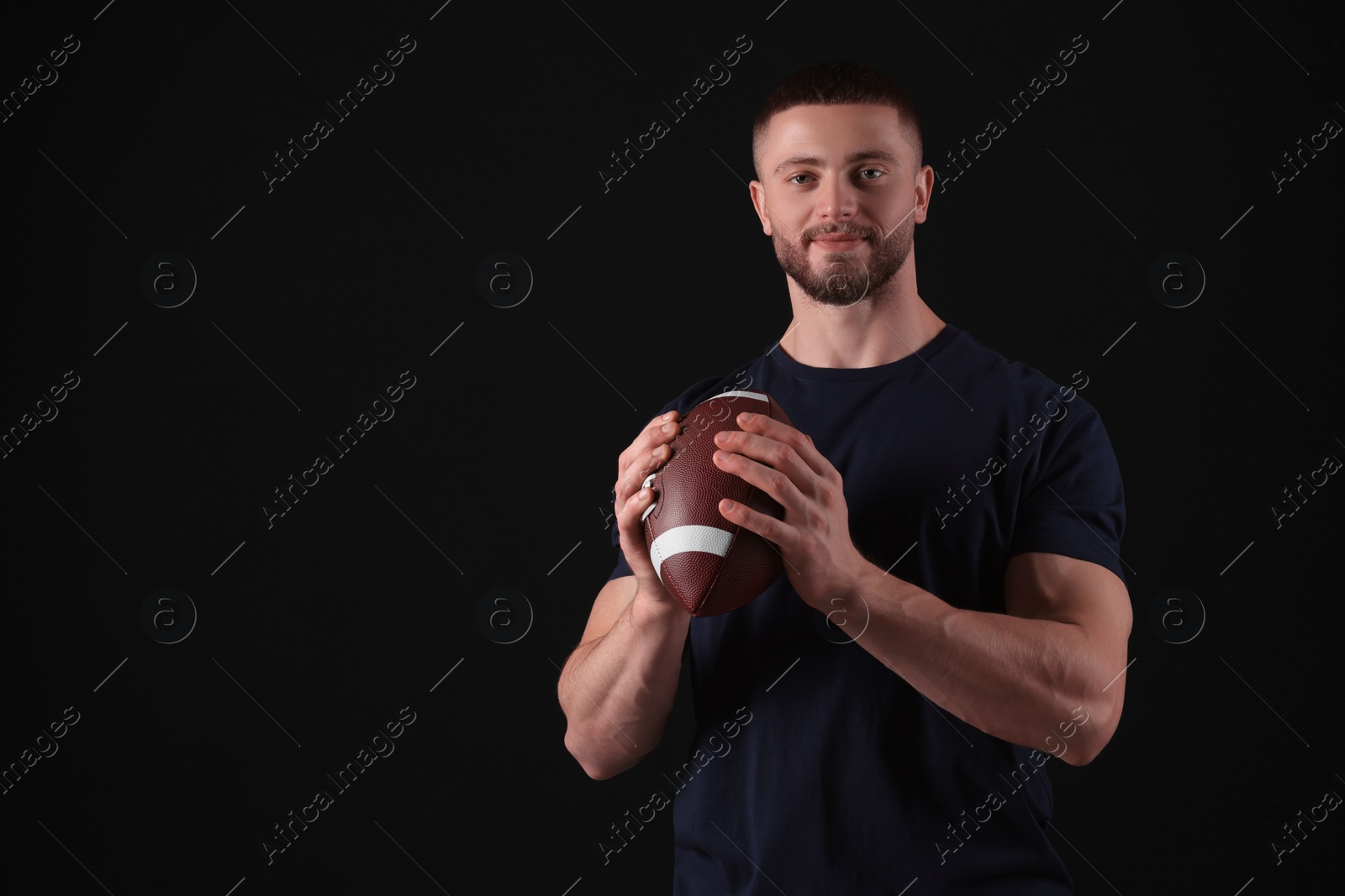 Photo of Athletic young man with American football ball on black background. Space for text