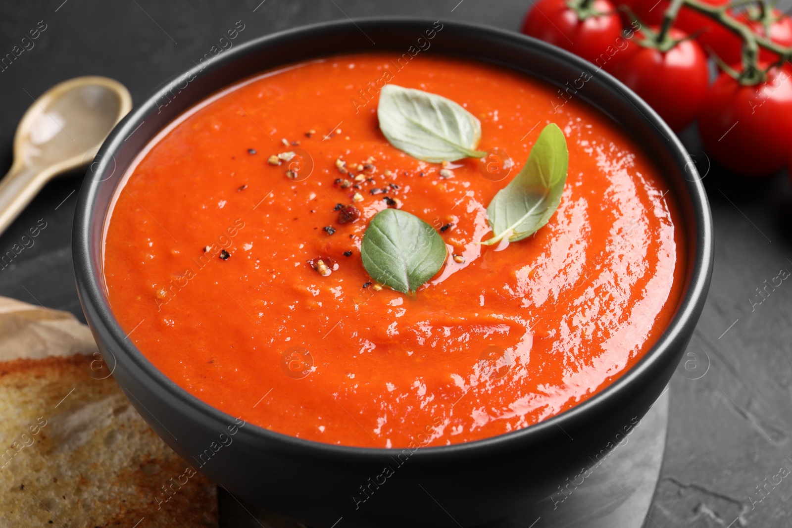 Photo of Delicious tomato cream soup served on black textured table, closeup