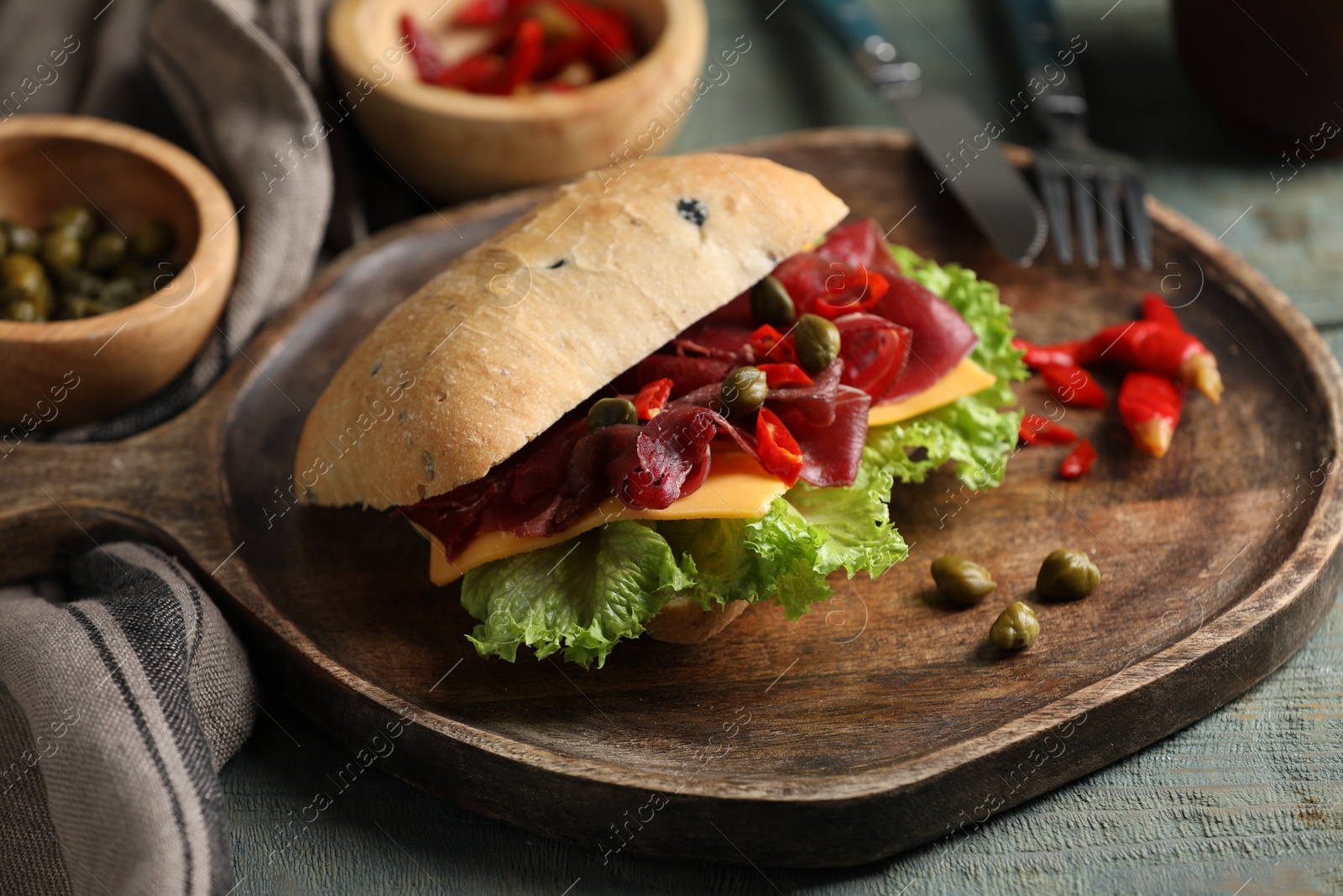 Photo of Delicious sandwich with bresaola, cheese and lettuce served on light blue wooden table, closeup